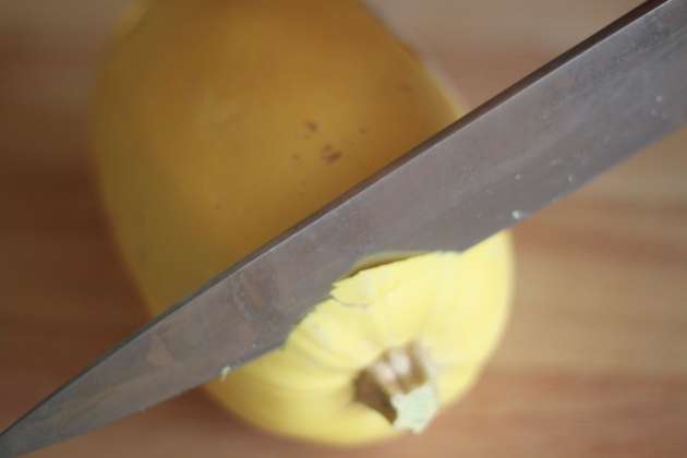 Large knife cutting off the stem end of a spaghetti squash