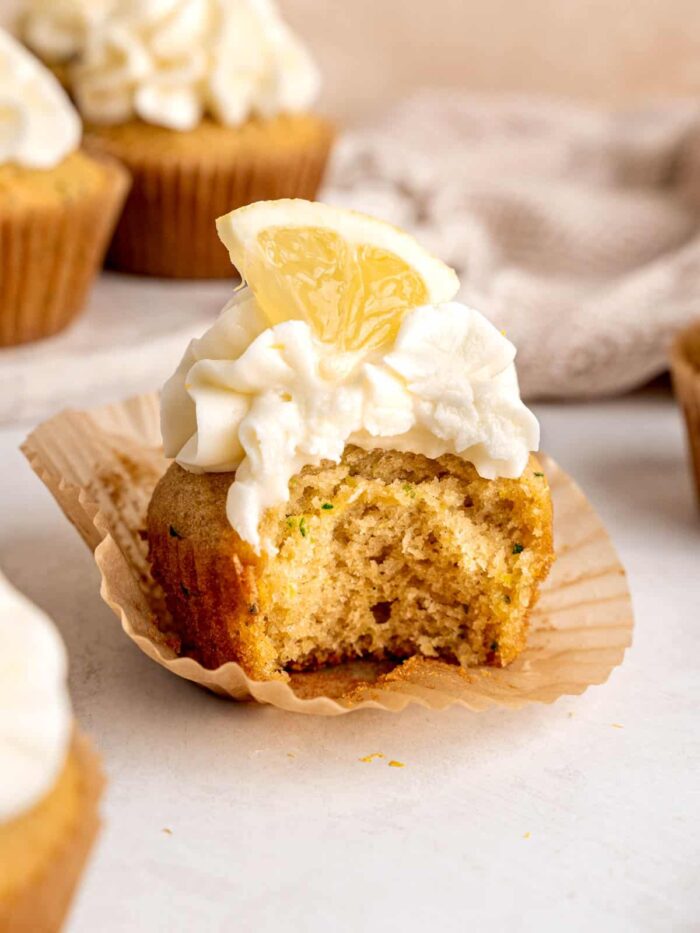 A lemon zucchini cupcake with a bite, vanilla frosting, and a lemon wedge for garnish