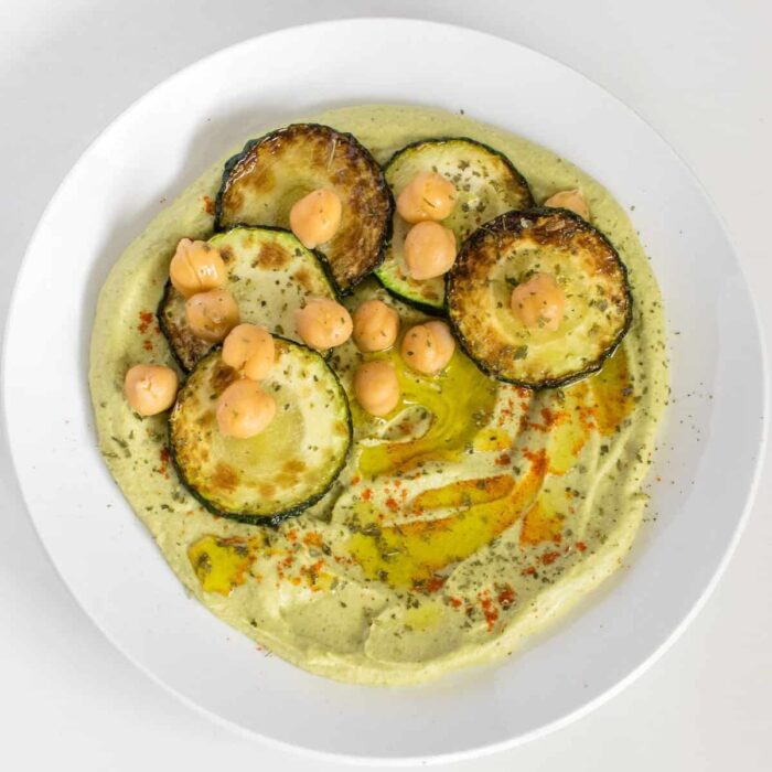 a bowl of zucchini hummus with sautéed zucchini, chickpeas, and a drizzle of olive oil