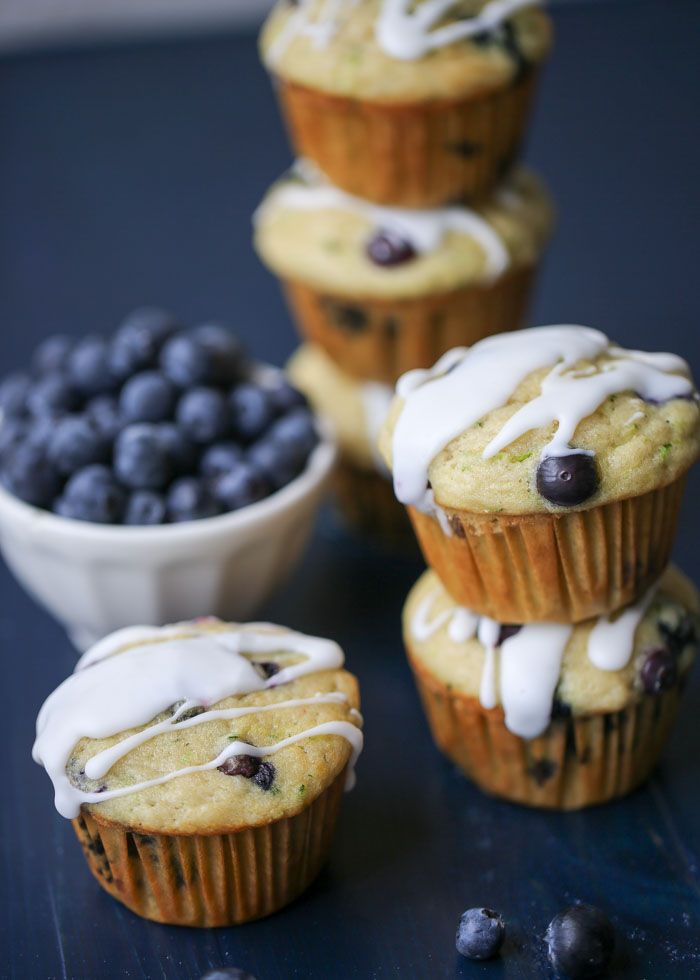 Several stacks of Lemon Blueberry Zucchini Muffins with a bowl of blueberries in the background