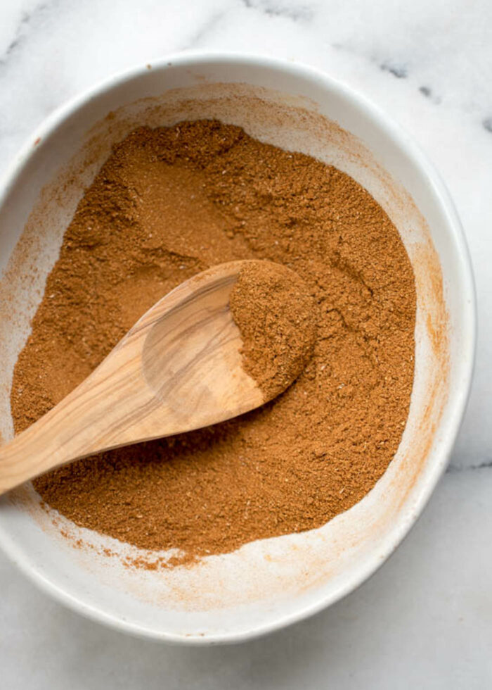 A bowl of pumpkin pie spice mix with a small wooden spoon in it