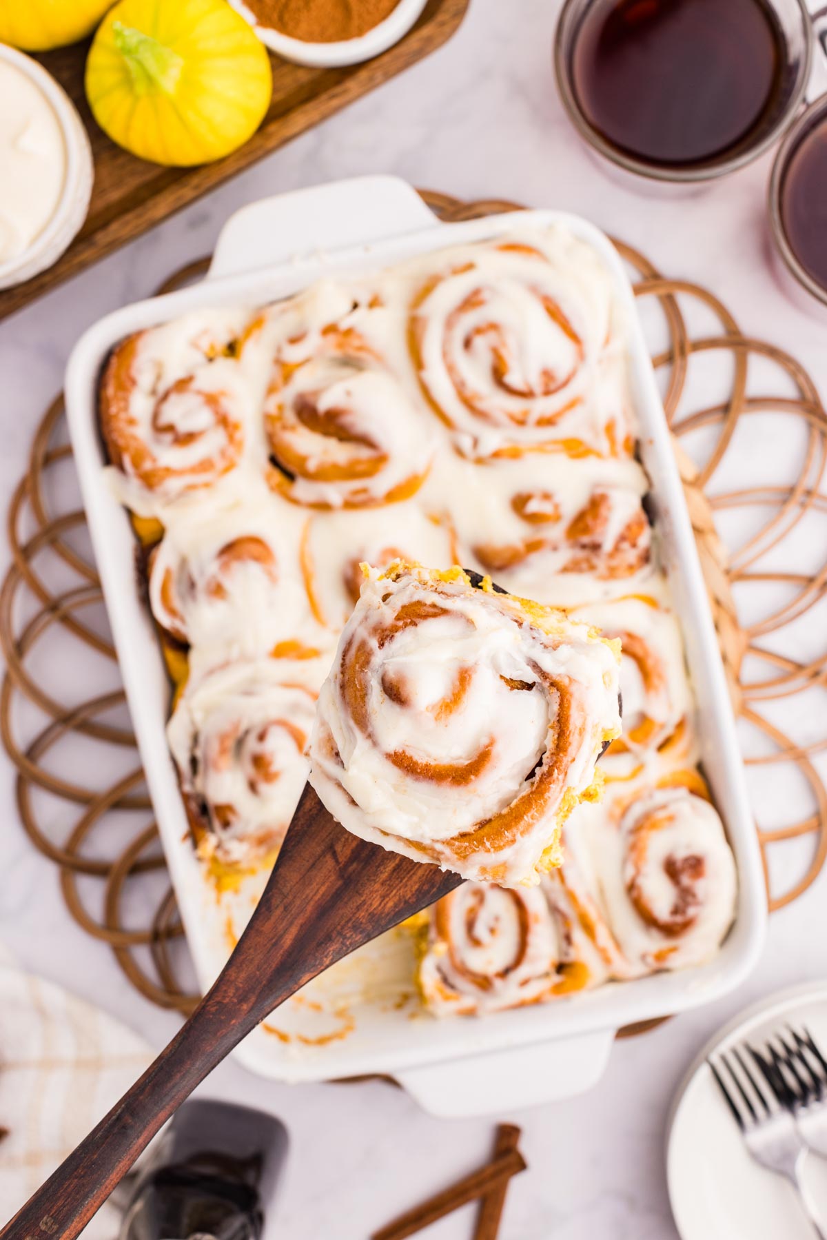 a wooden spoon lifts a pumpkin cinnamon roll out of its pan