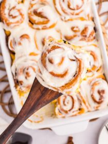 a wooden spoon lifts a pumpkin cinnamon roll from the pan